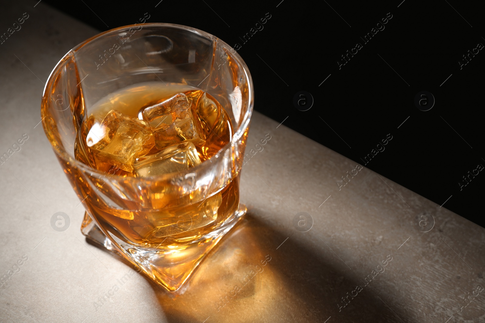 Photo of Golden whiskey in glass with ice cubes on table. Space for text