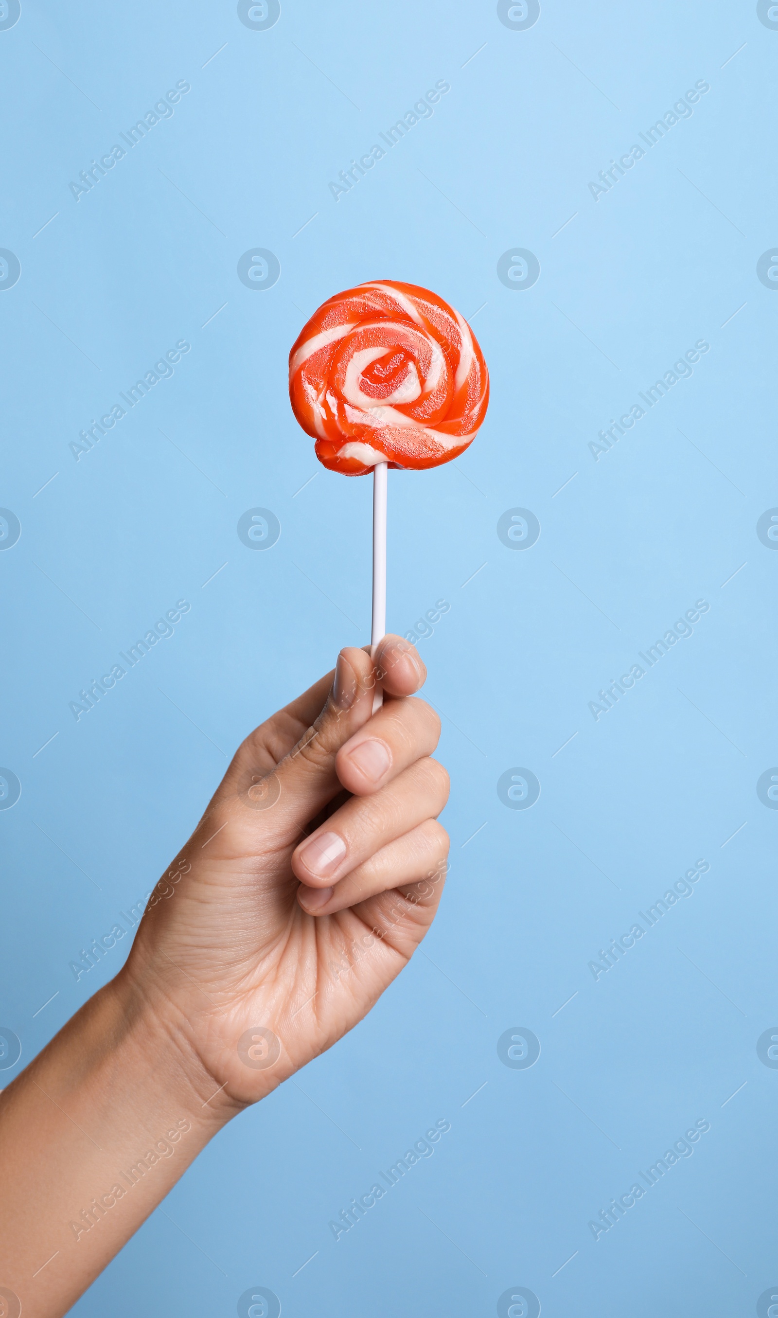 Photo of Woman holding bright tasty lollipop on light blue background, closeup