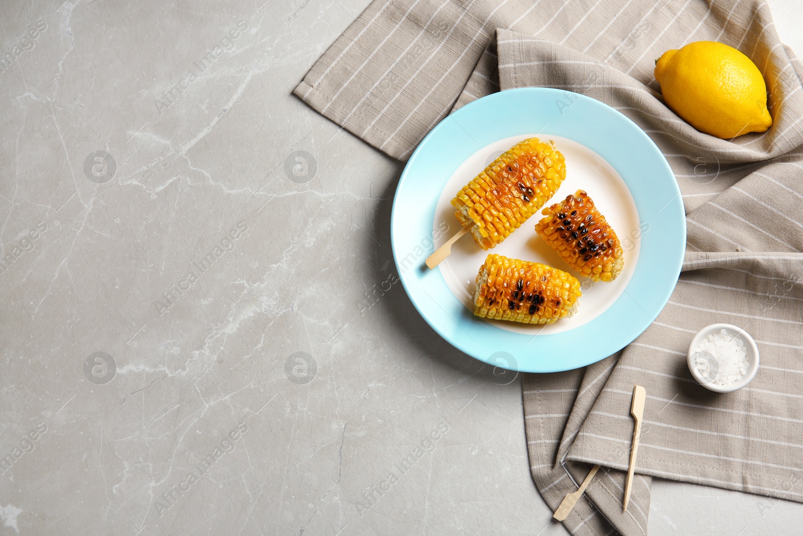 Photo of Plate with delicious grilled corn cobs on light table, top view. Space for text