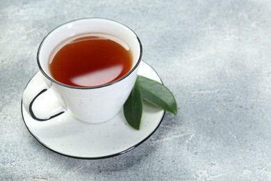 Photo of Aromatic tea in cup and green leaves on grey table. Space for text