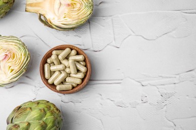 Photo of Bowl with pills and fresh artichokes on white textured table, flat lay. Space for text