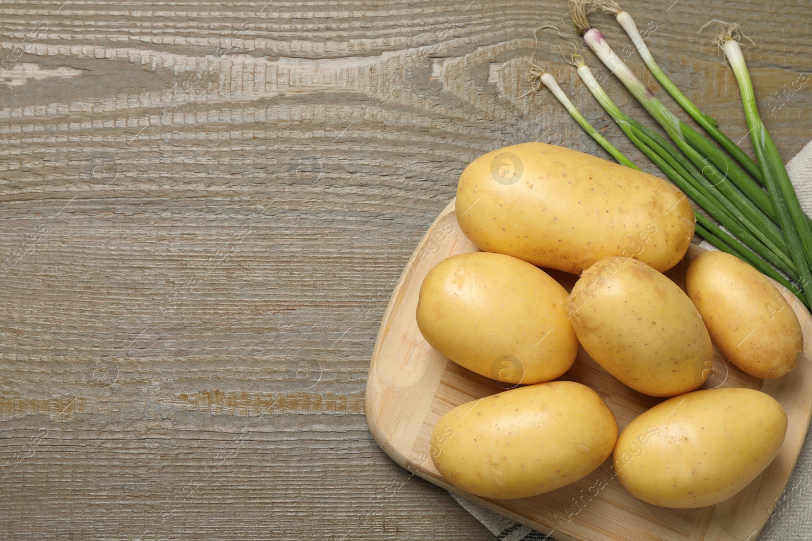 Photo of Fresh raw potatoes and green onions on wooden table, flat lay. Space for text