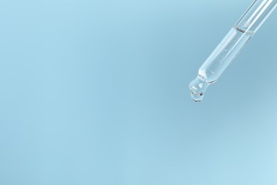 Photo of Dripping cosmetic serum from pipette on light blue background, space for text