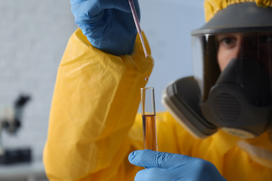 Scientist in chemical protective suit dripping reagent  into test tube at laboratory, focus on hands. Virus research