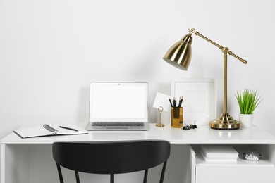 Cozy workspace with laptop, lamp and stationery on wooden desk at home