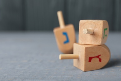 Photo of Hanukkah traditional dreidels with letters Gimel and He on grey wooden table, closeup. Space for text