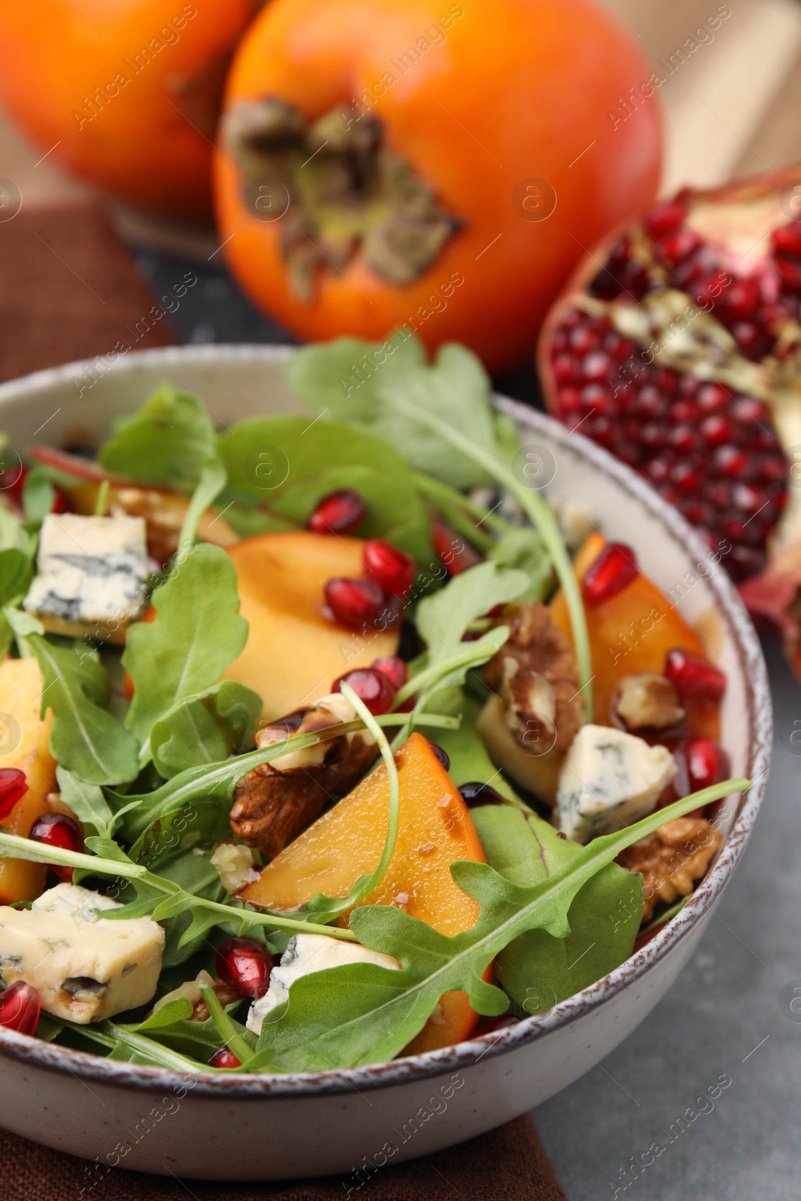 Photo of Tasty salad with persimmon, blue cheese, pomegranate and walnuts served on light grey table, closeup