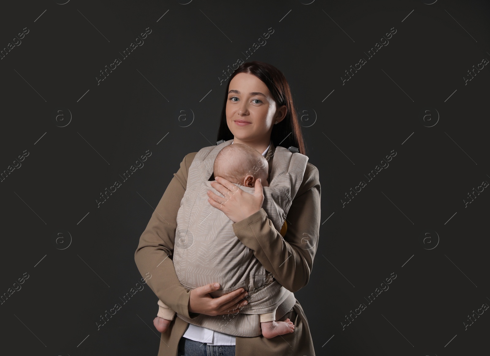 Photo of Mother holding her child in baby carrier on black background