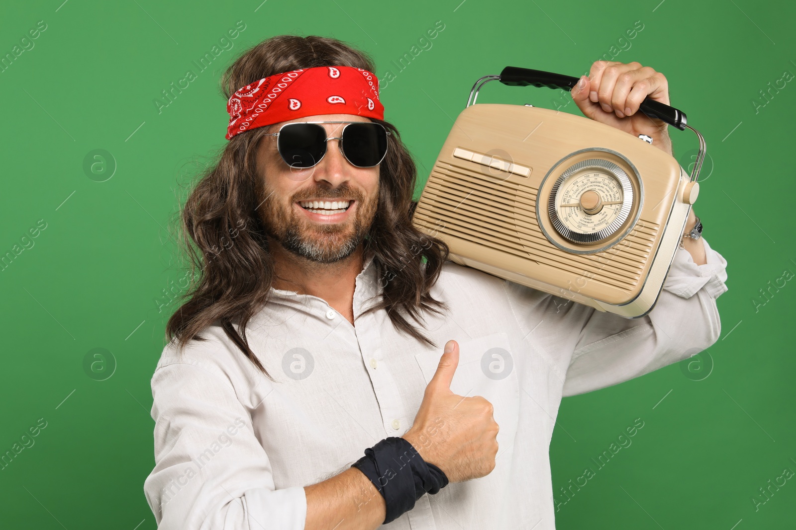 Photo of Stylish hippie man with radio showing thumbs up on green background