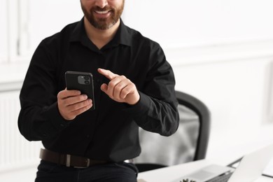 Smiling man using smartphone in office, closeup. Space for text