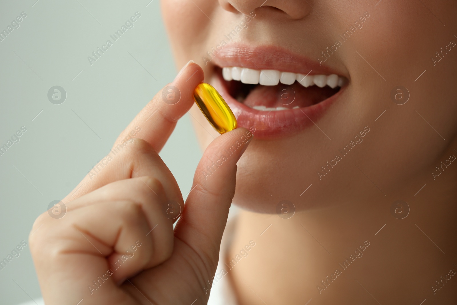 Photo of Young woman taking dietary supplement pill on blurred background, closeup