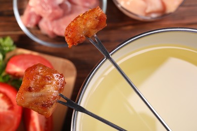 Fondue pot, forks with fried meat pieces and other products on wooden table, closeup