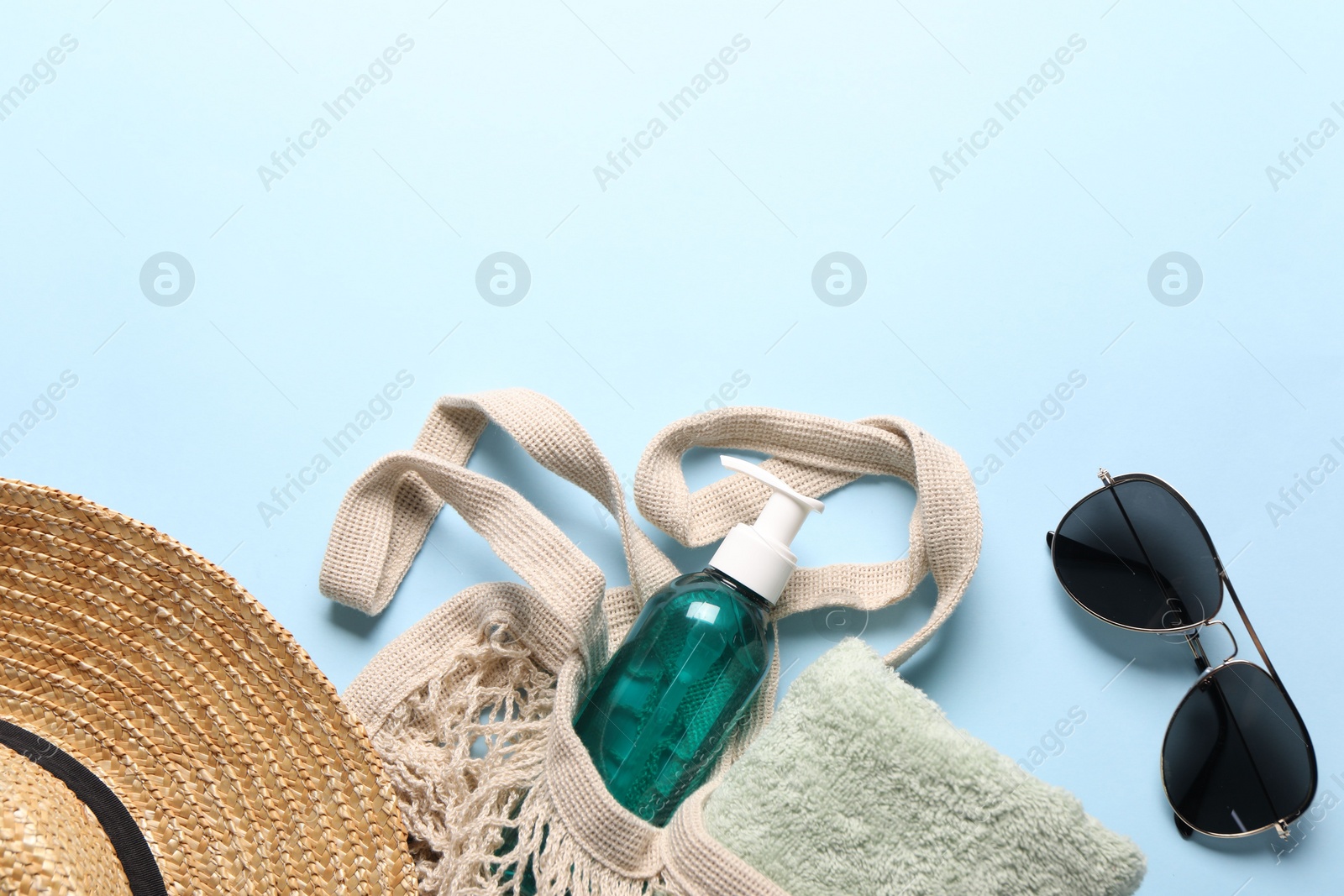 Photo of String bag, sunglasses, towel, straw hat and cosmetic product on light blue background, top view. Space for text