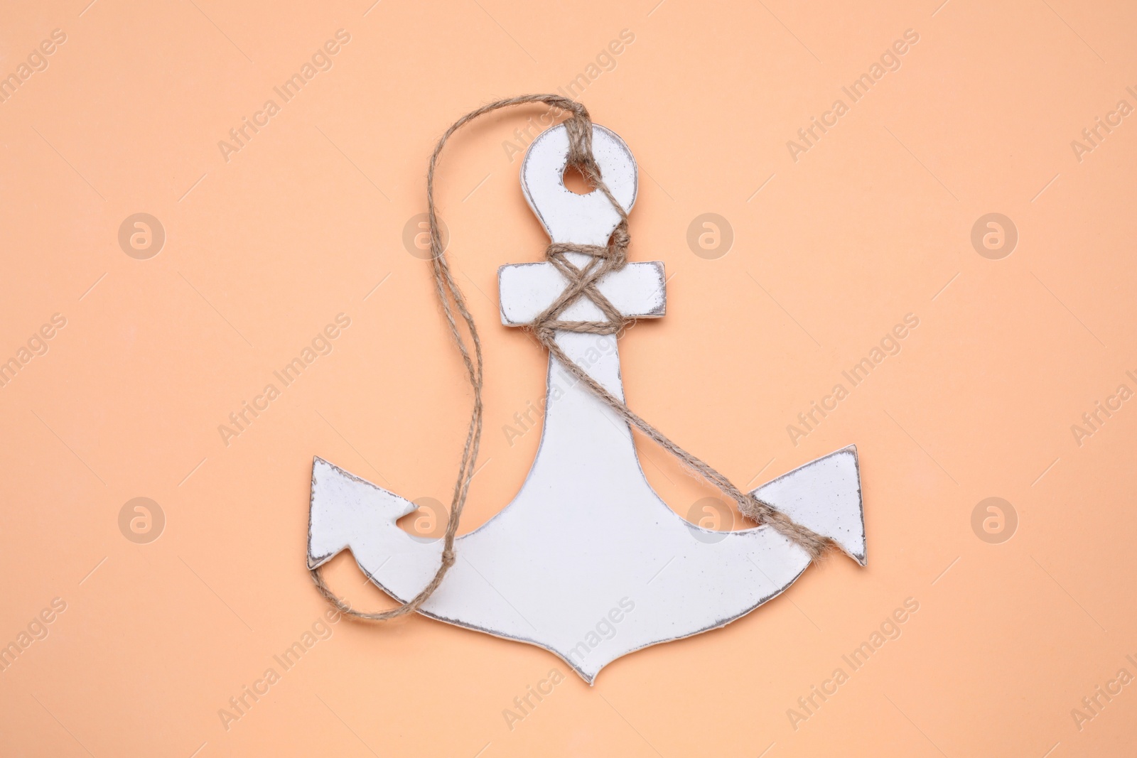 Photo of White wooden anchor figure on pale orange background, top view