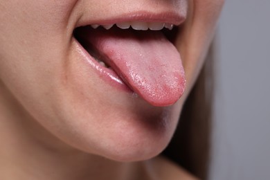 Closeup view of woman showing her tongue on grey background