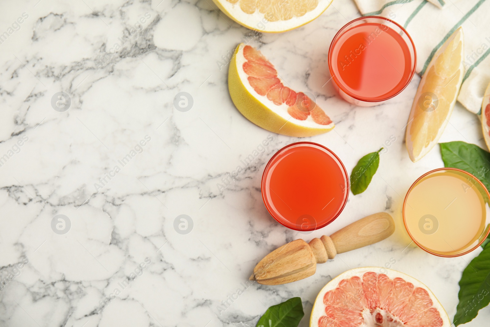 Photo of Glasses of different pomelo juices and fruits on white marble table, flat lay. Space for text