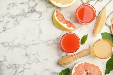 Glasses of different pomelo juices and fruits on white marble table, flat lay. Space for text