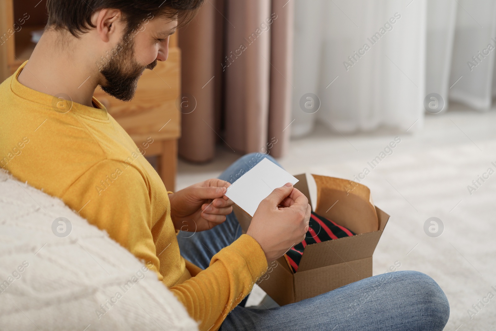 Photo of Happy man with greeting card near parcel at home. Internet shopping