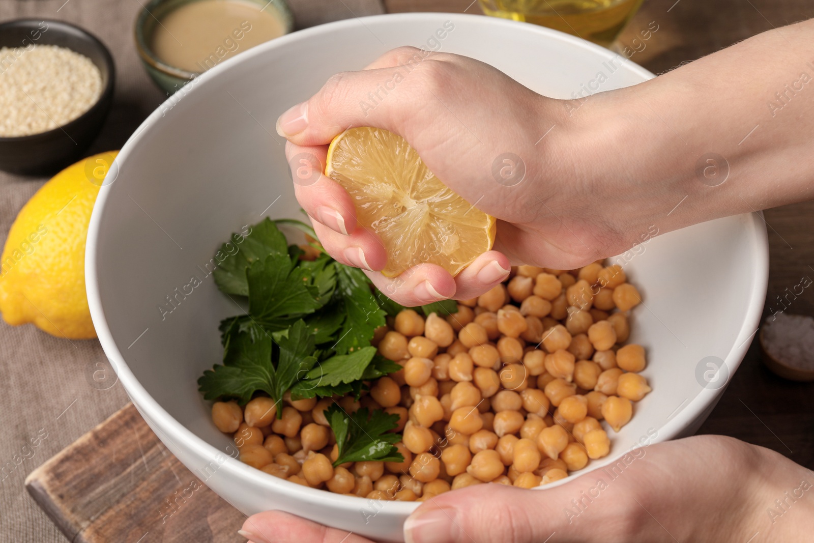 Photo of Woman squeezing lemon juice onto chickpeas at table, closeup. Cooking delicious hummus