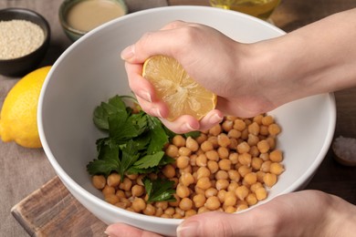 Photo of Woman squeezing lemon juice onto chickpeas at table, closeup. Cooking delicious hummus