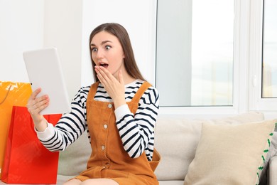 Special Promotion. Emotional woman looking at tablet on sofa indoors, space for text