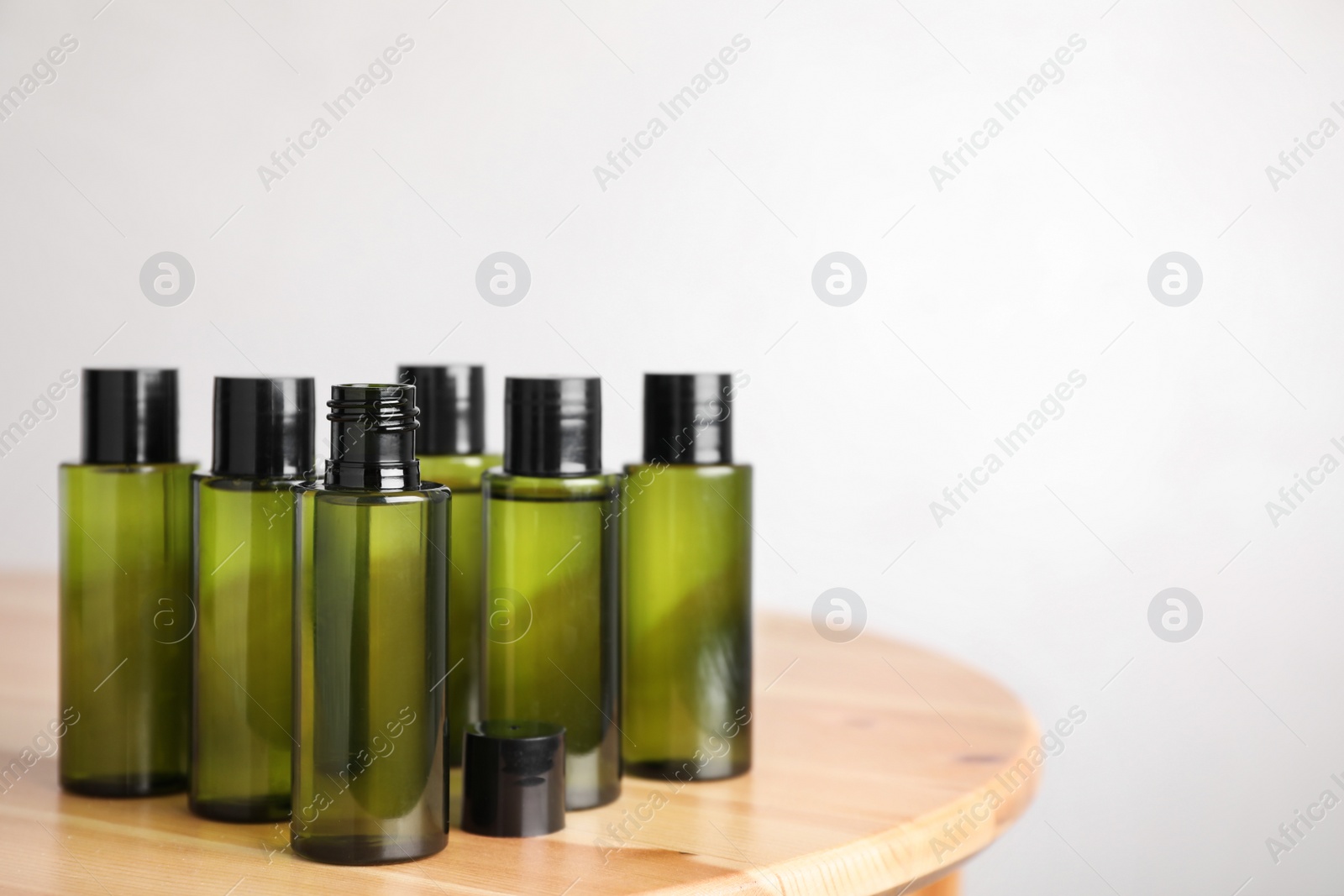 Photo of Mini bottles with cosmetic products on wooden table against light background. Space for text