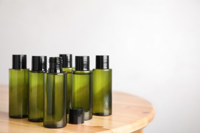 Mini bottles with cosmetic products on wooden table against light background. Space for text