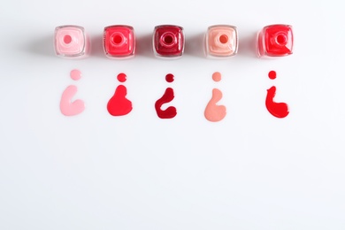 Photo of Spilled colorful nail polishes and bottles on white background, top view