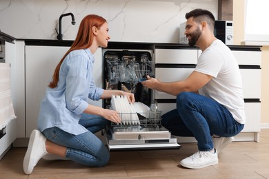 Happy couple loading dishwasher with plates in kitchen