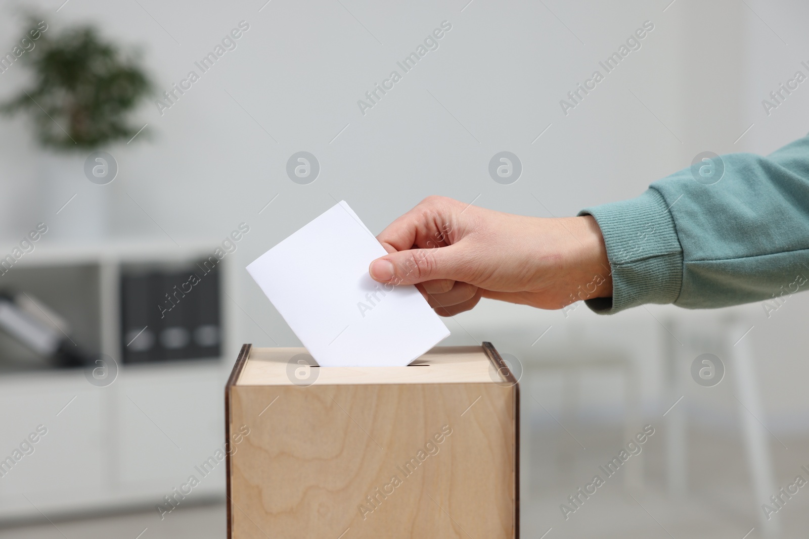 Photo of Woman putting her vote into ballot box on blurred background, closeup