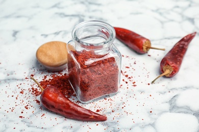 Photo of Jar with crushed chili pepper and pods on light background