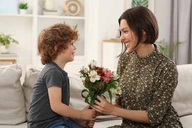 Happy woman with her cute son and bouquet of beautiful flowers at home. Mother's day celebration