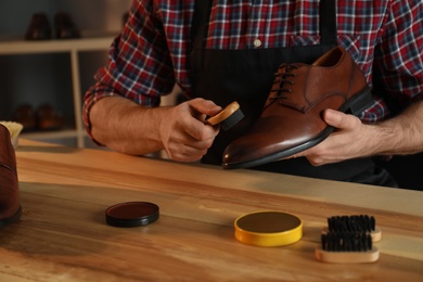 Photo of Craftsman taking professional care of brown leather shoe in workshop, closeup