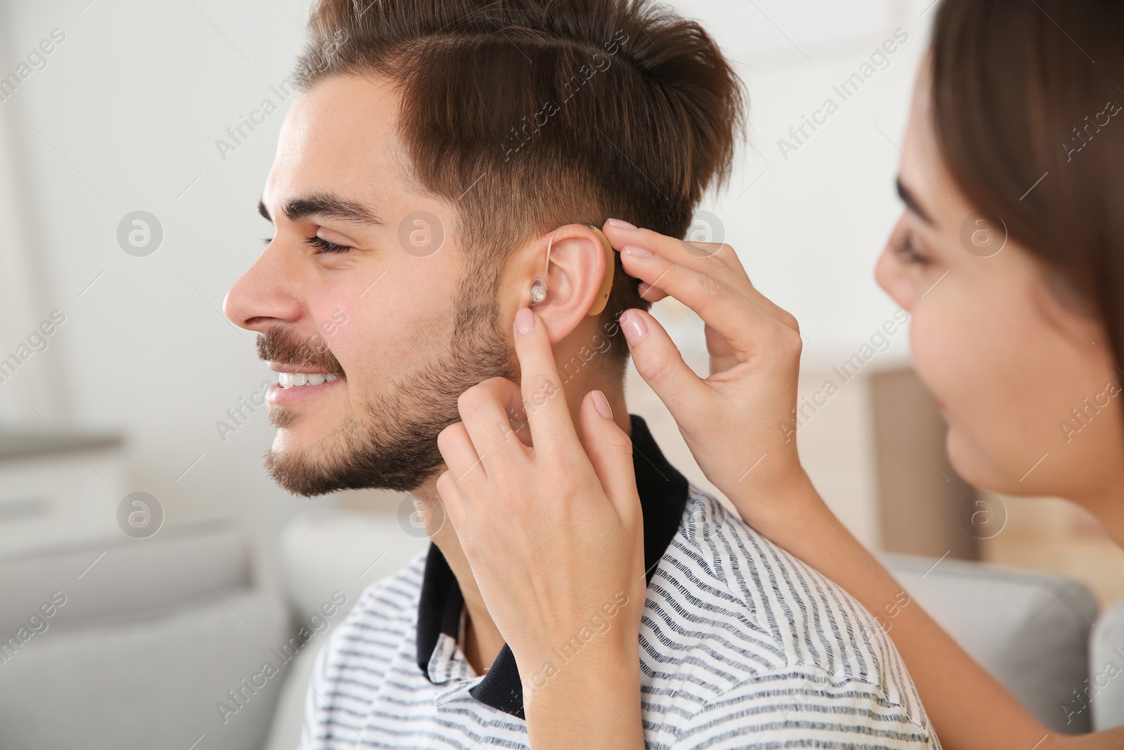 Photo of Woman putting hearing aid in man's ear indoors