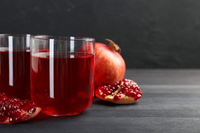 Photo of Tasty pomegranate juice in glasses and fresh fruits on black wooden table, closeup. Space for text