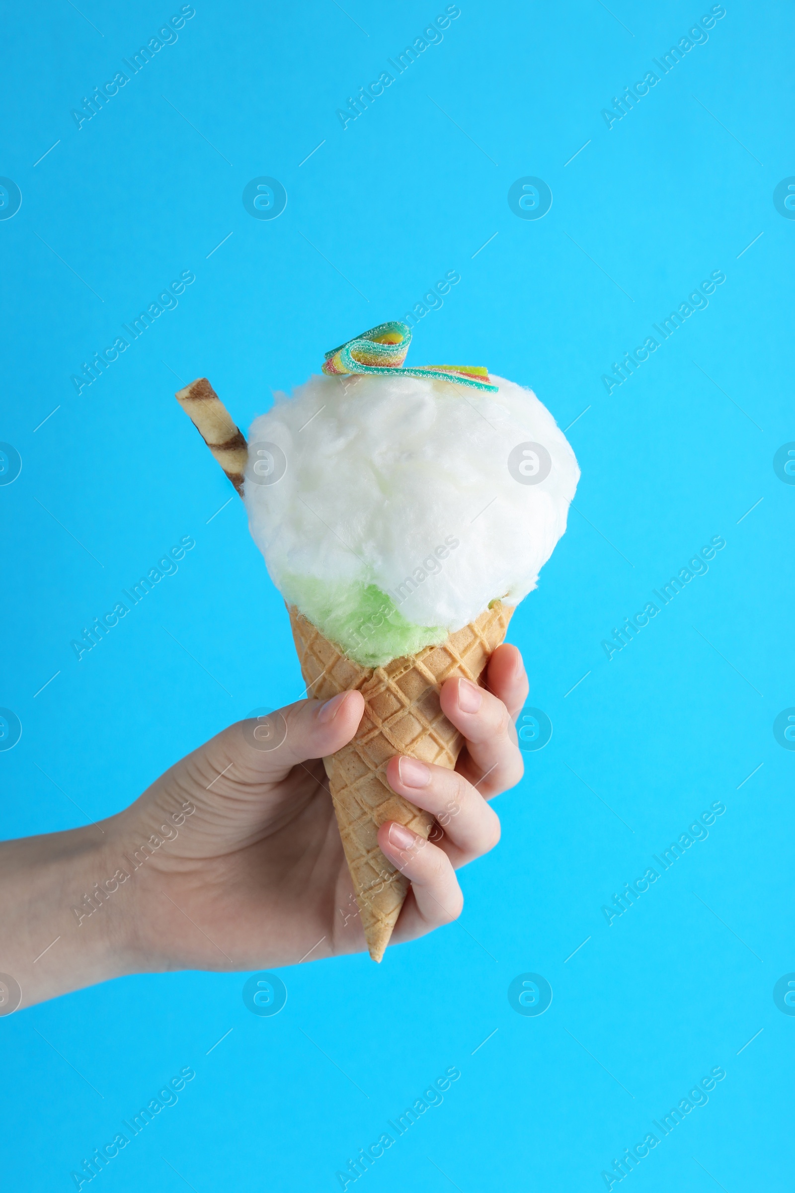 Photo of Woman holding waffle cone with cotton candy on light blue background, closeup