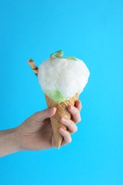 Woman holding waffle cone with cotton candy on light blue background, closeup