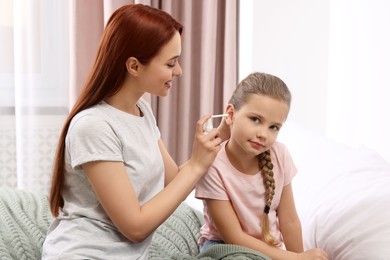 Photo of Mother spraying medication into daughter's ear in bedroom