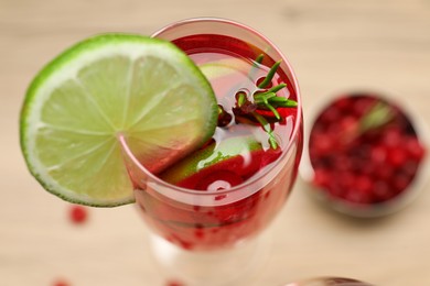 Photo of Tasty cranberry cocktail with rosemary and lime in glass on beige table, closeup