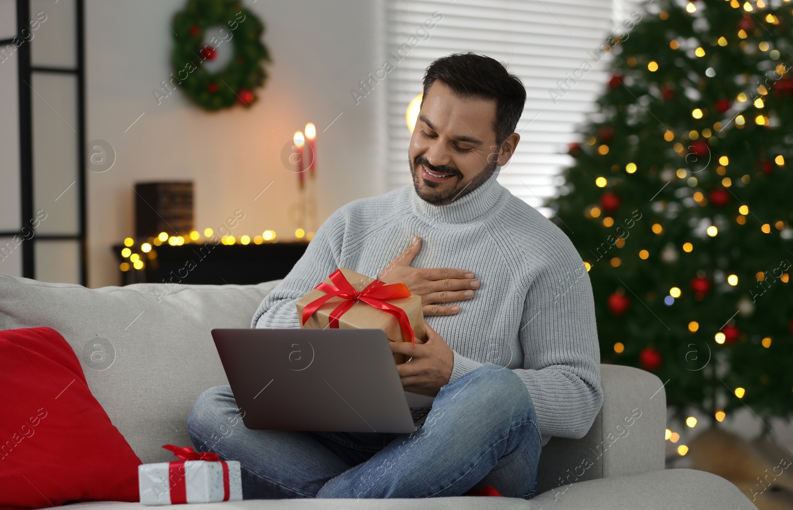 Photo of Celebrating Christmas online with exchanged by mail presents. Man thanking for gift during video call on laptop at home