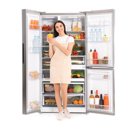 Young woman with bell pepper near open refrigerator on white background
