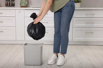 Photo of Woman taking garbage bag out of trash bin in kitchen, closeup