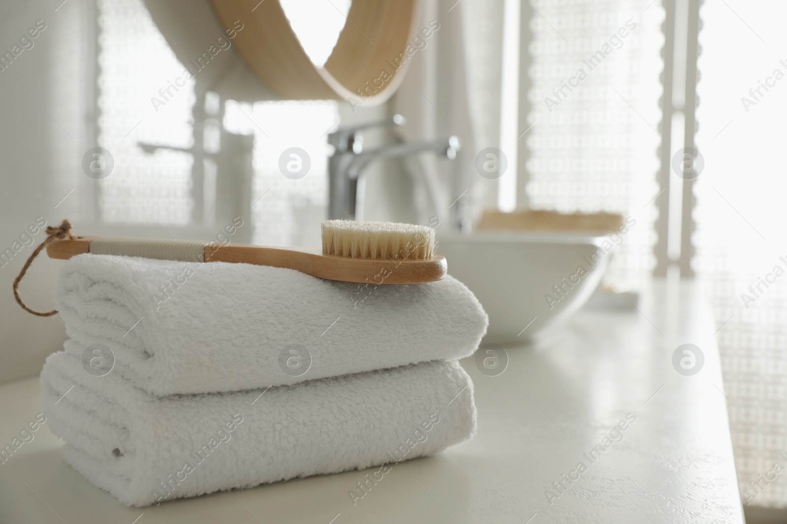 Photo of Stack of clean towels and massage brush on countertop in bathroom. Space for text
