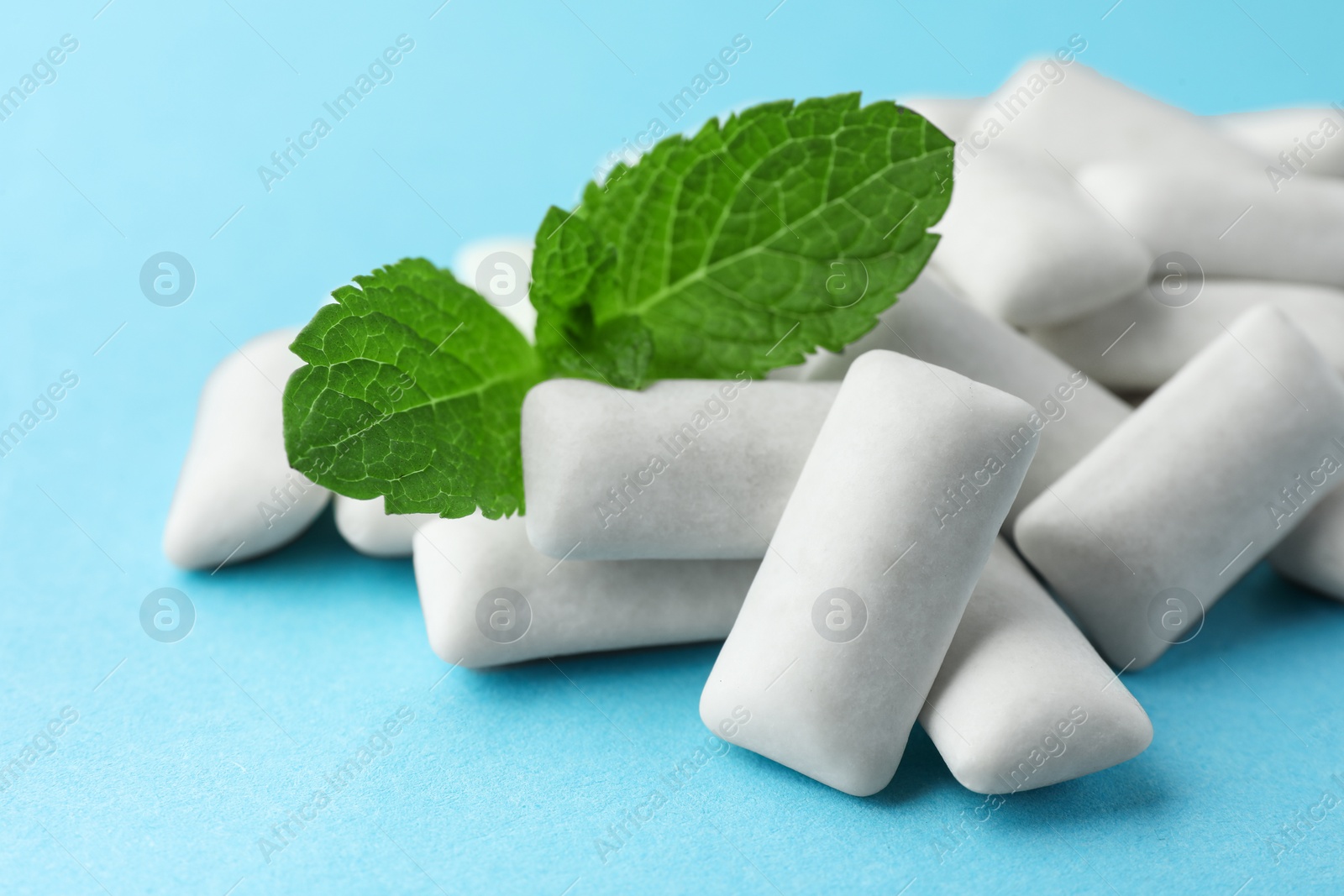 Photo of Pile of tasty white chewing gums and mint leaves on light blue background, closeup