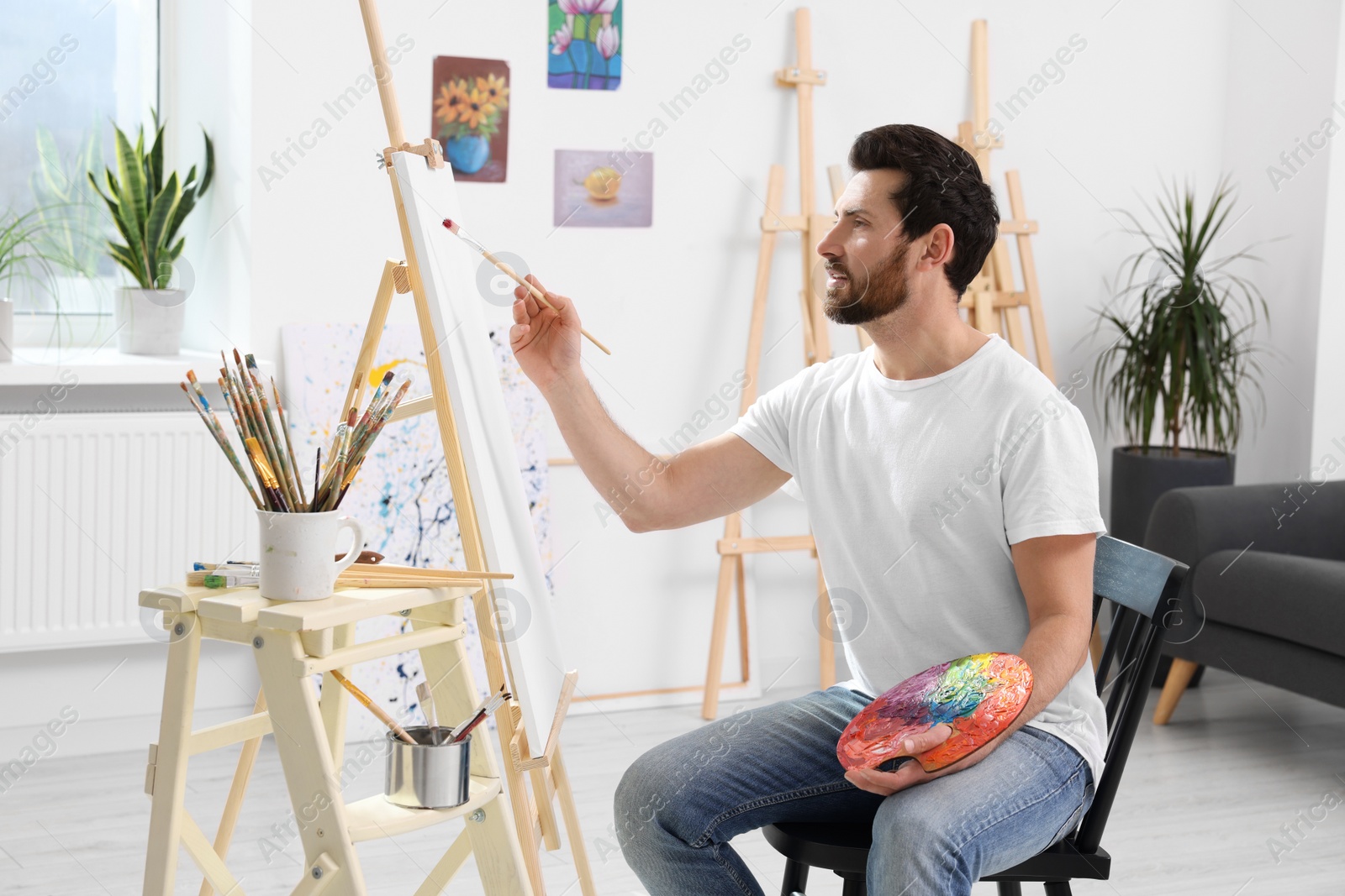 Photo of Man painting in studio. Using easel to hold canvas