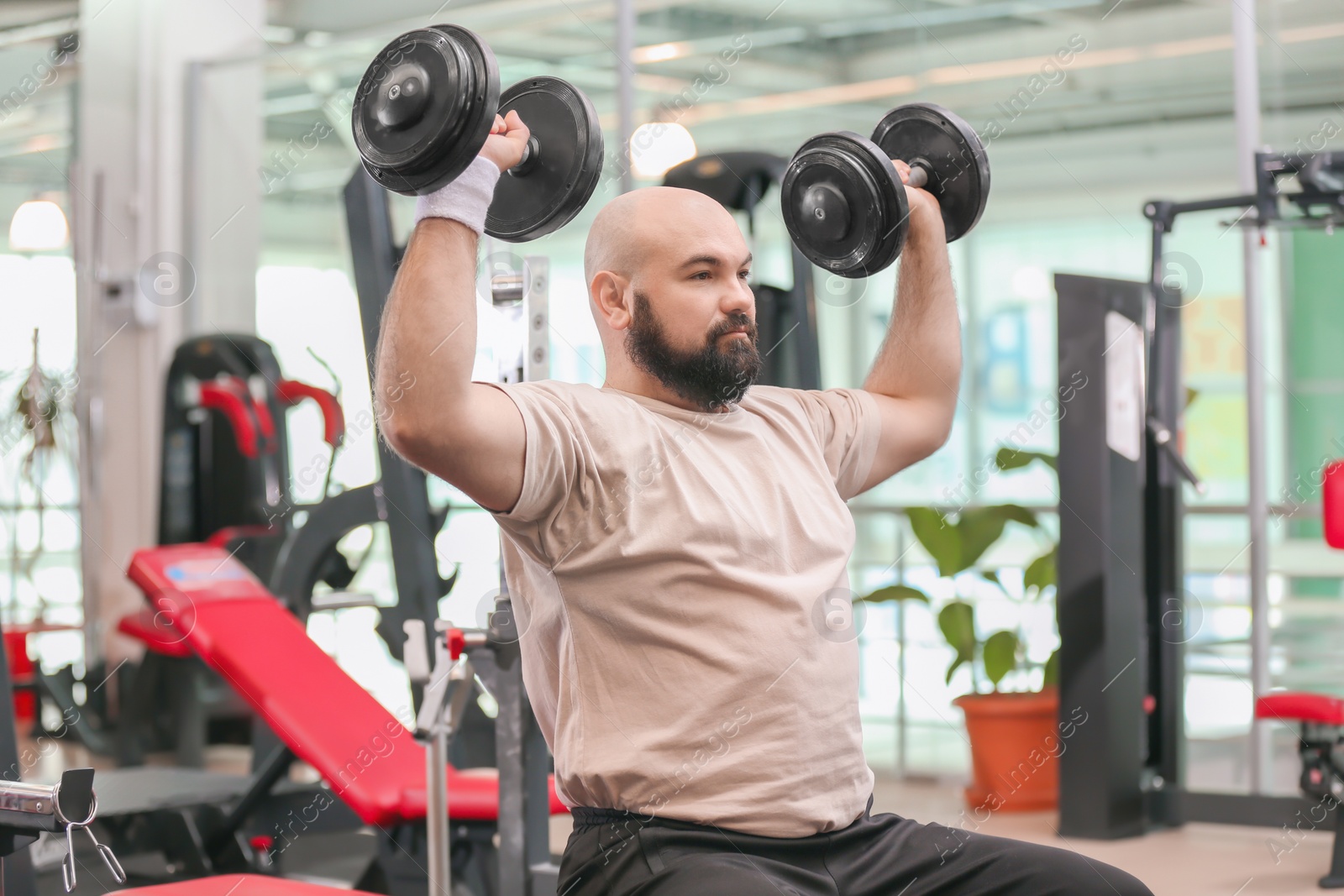 Photo of Overweight man training with dumbbells in gym