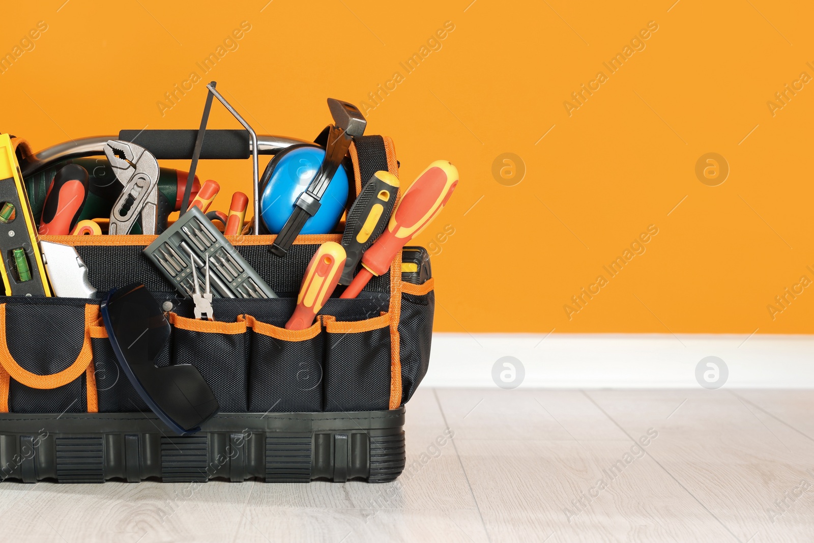 Photo of Bag with different tools for repair on floor near orange wall. Space for text