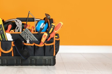 Bag with different tools for repair on floor near orange wall. Space for text