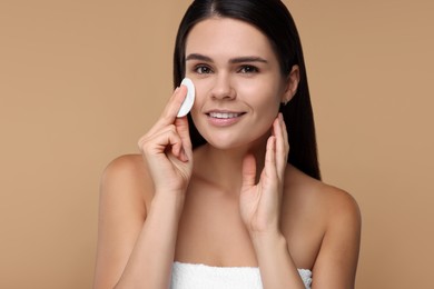 Photo of Young woman cleaning her face with cotton pad on beige background