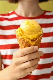 Woman holding tasty ice cream in wafer cone on yellow background, closeup